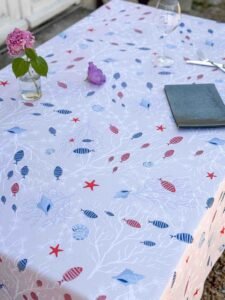 Nappe polyester Moana – motif marin poissons, étoiles de mer et coraux, coloris beige ou bleu, disponible en ronde, ovale, carrée ou rectangulaire