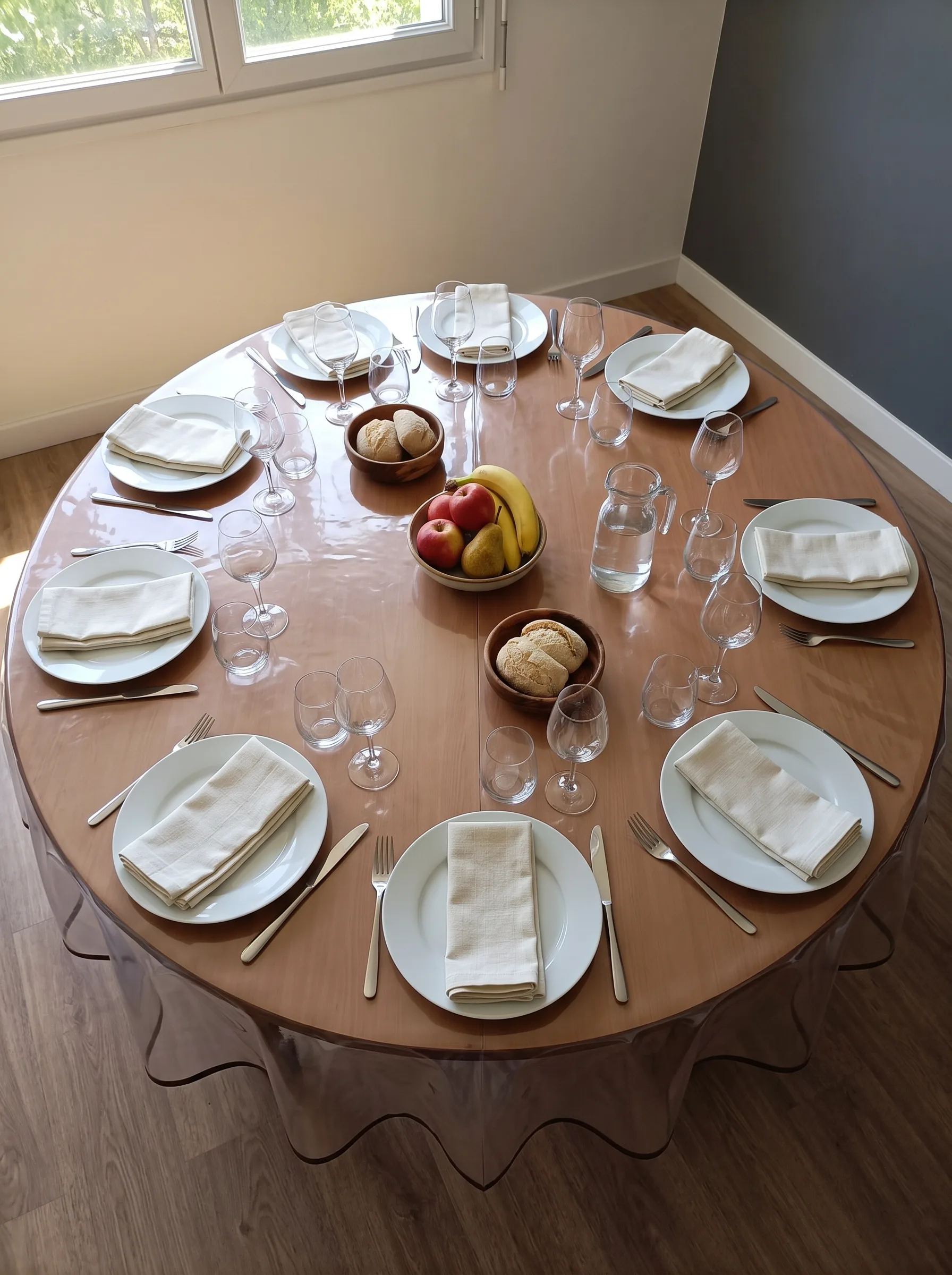 Toile cirée transparente ronde sur grande table ronde en bois dressée pour huit personnes vue du dessus – protection invisible laissant apparaître le bois chaud, biais gris ondulé visible sur le pourtour, salle à manger lumineuse