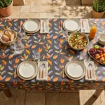 Toile cirée déco Alice 140 cm – feuillage stylisé en orange brûlé, jaune ocre et vert sauge sur fond anthracite profond, vendue au mètre ou sur mesure