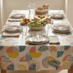 Toile cirée déco Printanière 140 cm – grandes feuilles de palmier et monstera en rose corail, bleu canard et jaune soleil sur fond blanc, vendue au mètre ou sur mesure