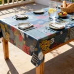 Toile cirée déco Printo 140 cm – patchwork tropical mêlant monstera, palmes et fleurs stylisées en jaune moutarde, rouge corail et blanc sur fond bleu pétrole, vendue au mètre ou sur mesure