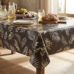 Toile cirée déco Ramage terre 140 cm – foisonnement de palmes fines et feuilles d'olivier en blanc nacré et or champagne sur fond gris taupe, vendue au mètre ou sur mesure