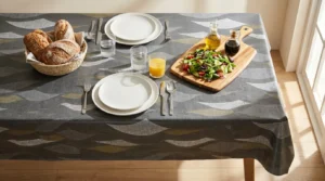 Toile cirée déco Sabine 140 cm – grandes feuilles lancéolées gris argent et or kaki sur fond anthracite texturé, vendue au mètre ou sur mesure