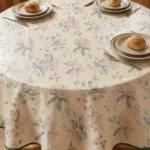 Toile cirée ronde Paula 160 cm – motif botanique fleurs rose poudré et feuillages bleu-gris aquarelle sur fond crème ivoire
