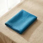 Serviette coton bleu paon pliée sur nappe beige – lumière naturelle douce