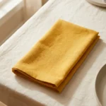 Serviette coton jaune curry pliée sur nappe blanche – table dressée lumière naturelle