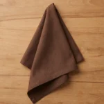 Serviette coton chocolat pliée en triangle vue de dessus sur table bois clair