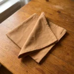 Serviettes coton caramel pliées sur table en bois brut – ambiance naturelle et chaleureuse