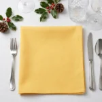 Serviette coton jaune poussin pliée à plat sur table dressée décor de Noël houx et pommes de pin