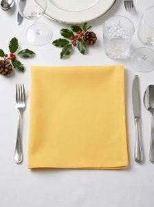 Serviette coton jaune poussin pliée à plat sur table dressée décor de Noël houx et pommes de pin