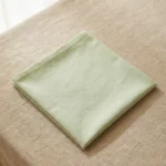 Serviette coton vert céladon pliée sur nappe lin beige – ambiance naturelle