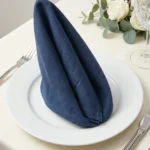 Serviettes coton bleu navy pliées en pile sur nappe blanche – table dressée vaisselle dorée