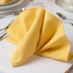 Serviette de table coton jaune poussin pliée en éventail sur assiette – table dressée bougies