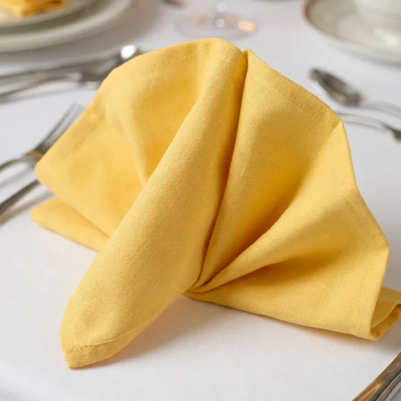 Serviette de table coton jaune poussin pliée en éventail sur assiette – table dressée bougies