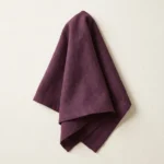 Serviette coton aubergine drapée sur fond blanc – détail tombé tissu coton