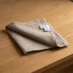 Serviette coton gris pliée sur table en chêne clair – vue de dessus lumière naturelle