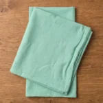 Serviettes coton vert d'eau pliées en pile sur table en bois clair – vue de dessus