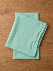 Serviettes coton vert d'eau pliées en pile sur table en bois clair – vue de dessus
