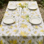 Toile cirée déco Mimosa blanc sur table rectangulaire dressée en extérieur – grappes de mimosa jaune doré et feuillages verts sur fond blanc, ambiance jardin printanier