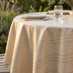 Toile cirée déco Riviera beige sur table ronde dressée – rayures fines argentées sur fond beige sable effet lin, ambiance intérieur chaleureux