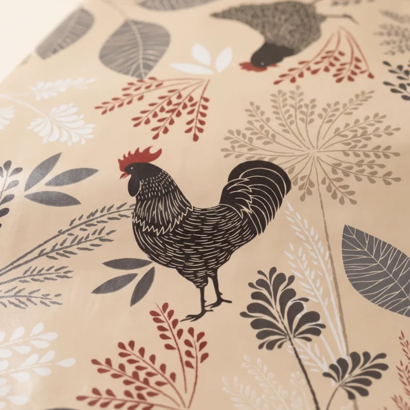 Gros plan sur le motif de la toile cirée déco Cotcot beige – coq dessiné à l'encre fine, crête rouge vif, feuillages graphiques gris anthracite et rouge bordeaux sur fond beige sable