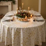 Toile cirée déco Étoile d'Or sur table ovale dressée pour Noël – motif étoiles dorées all-over fond blanc crème, bougies dorées et couronne végétale centrale, ambiance réveillon
