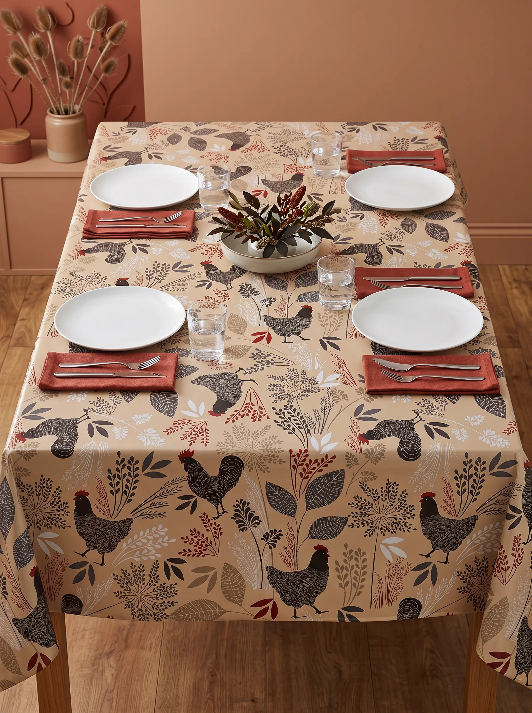 Toile cirée déco Cotcot beige sur table rectangulaire dressée – motif coqs et poules graphiques gris anthracite et rouge bordeaux sur fond beige sable, ambiance salle à manger terracotta