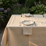 Toile cirée déco Riviera beige sur table rectangulaire dressée – rayures fines argentées sur fond beige sable effet lin, ambiance salle à manger épurée