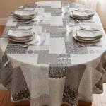 Toile cirée molletonné Dentelière gris sur table ovale dressée – motif patchwork dentelle et broderie gris anthracite et blanc sur fond gris perle