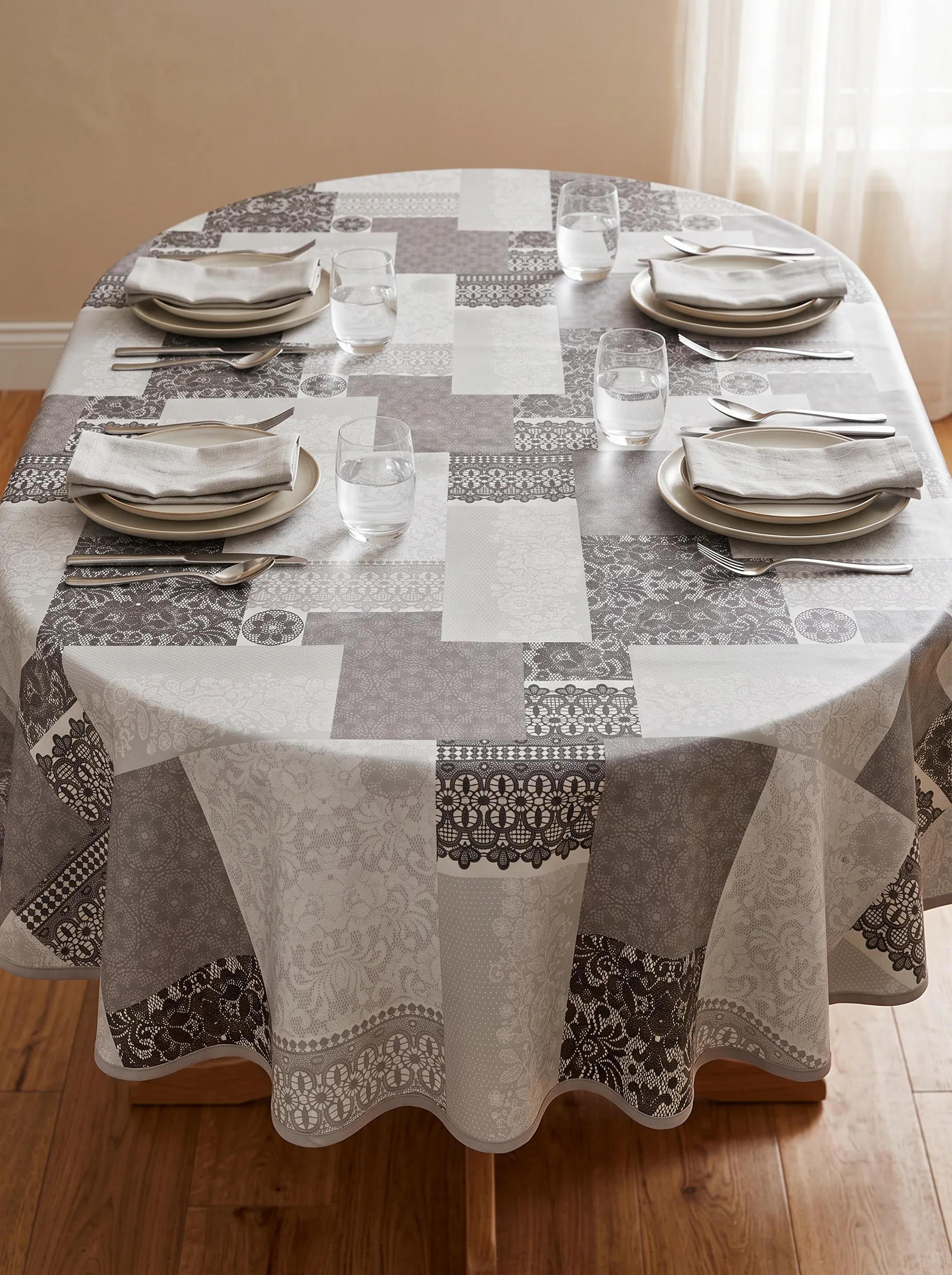 Toile cirée molletonné Dentelière gris sur table ovale dressée – motif patchwork dentelle et broderie gris anthracite et blanc sur fond gris perle