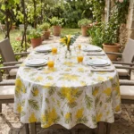 Toile cirée déco Mimosa blanc sur grande table ovale dressée en terrasse provençale – grappes de mimosa jaune doré et feuillages verts sur fond blanc, grande tablée estivale